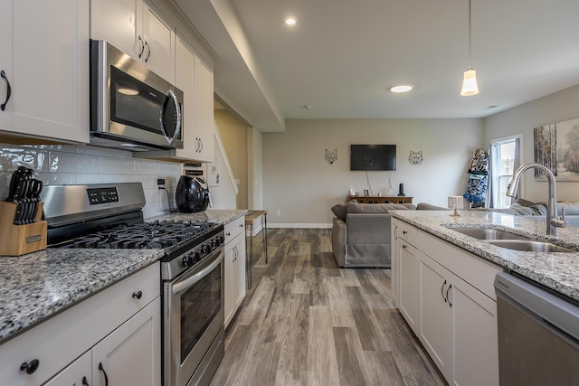 kitchen featuring a sink, dark wood finished floors, open floor plan, backsplash, and appliances with stainless steel finishes