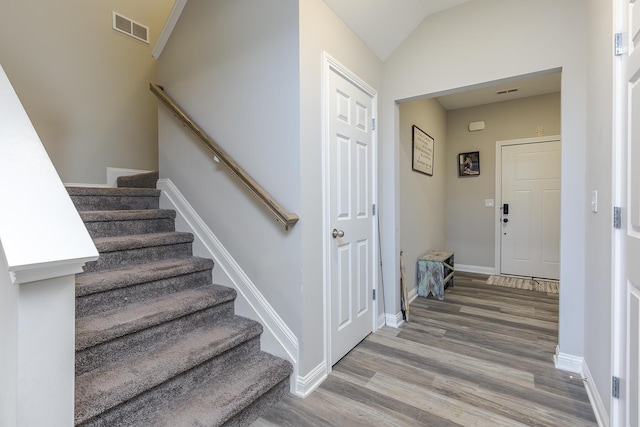 stairway with baseboards, wood finished floors, visible vents, and vaulted ceiling
