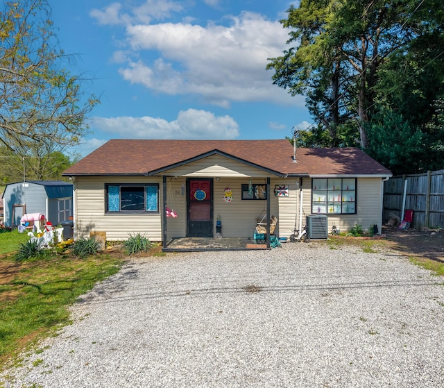view of front of property featuring a storage shed, central air condition unit, fence, an outbuilding, and gravel driveway