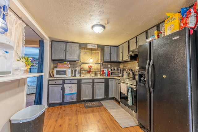 kitchen featuring a textured ceiling, light wood-type flooring, stainless steel electric range, white microwave, and black fridge with ice dispenser
