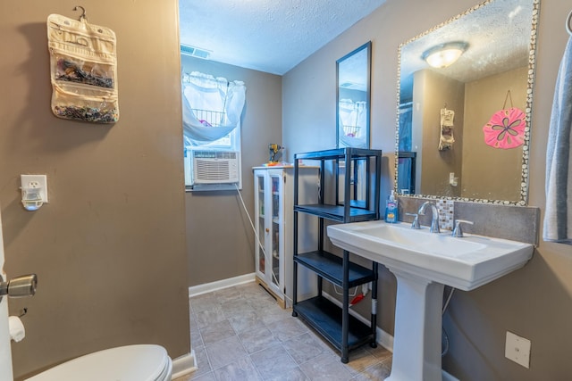 half bath with visible vents, toilet, cooling unit, baseboards, and a textured ceiling