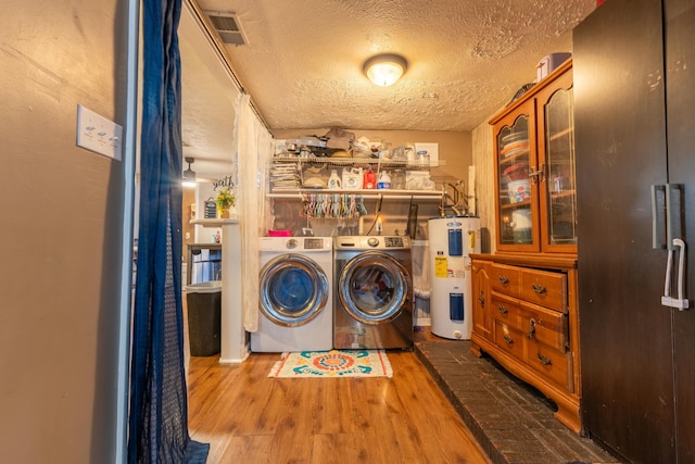 laundry room with a textured ceiling, electric water heater, visible vents, wood finished floors, and independent washer and dryer