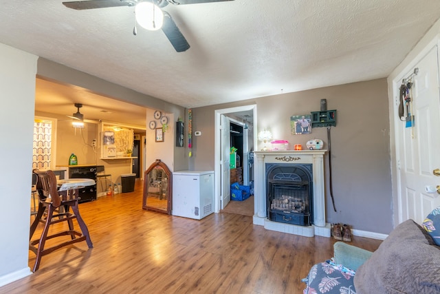 living room featuring baseboards, a ceiling fan, wood finished floors, and a fireplace with raised hearth