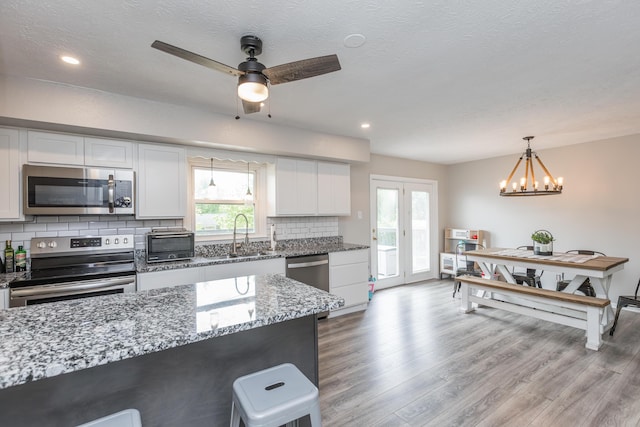 kitchen featuring white cabinets, a sink, light wood-style floors, stainless steel appliances, and decorative backsplash