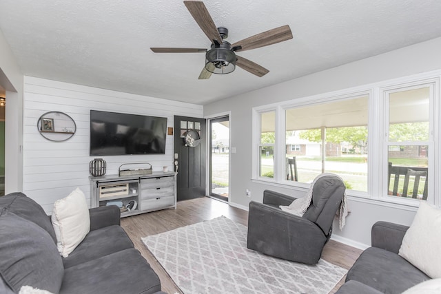 living room featuring baseboards, ceiling fan, a textured ceiling, and wood finished floors
