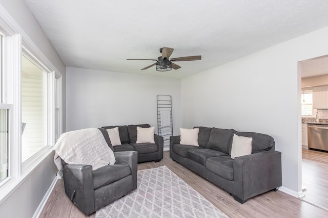 living area featuring a ceiling fan, baseboards, and light wood-style floors