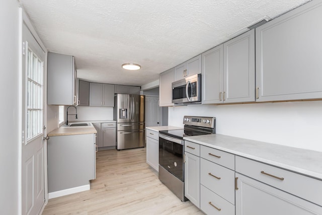 kitchen featuring light countertops, gray cabinets, a sink, light wood-style floors, and appliances with stainless steel finishes