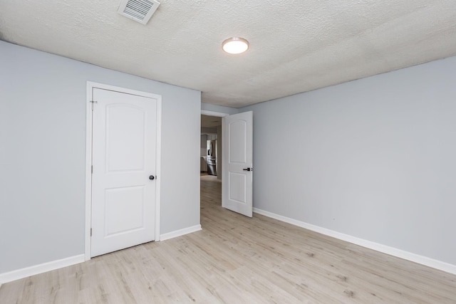 interior space featuring baseboards, light wood finished floors, a textured ceiling, and visible vents