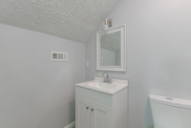 bathroom with vaulted ceiling, visible vents, toilet, vanity, and a textured ceiling