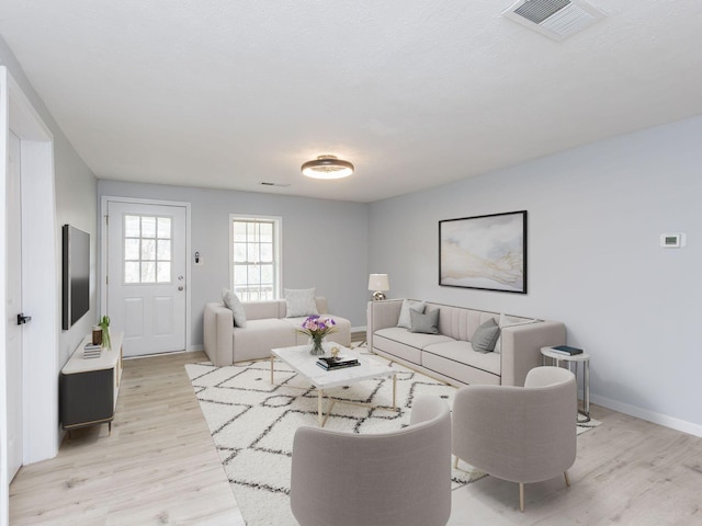 living room with light wood finished floors, baseboards, and visible vents