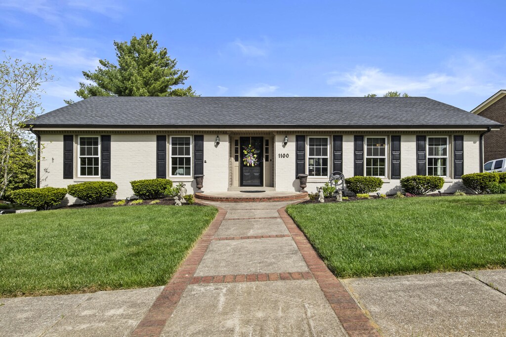 ranch-style home with a shingled roof, a front lawn, and brick siding