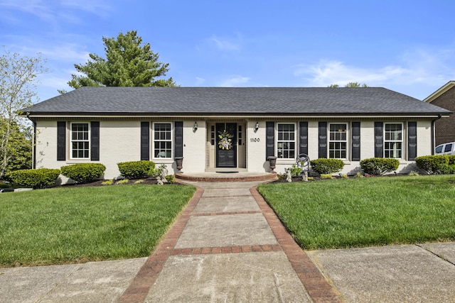 ranch-style home with a shingled roof, a front lawn, and brick siding