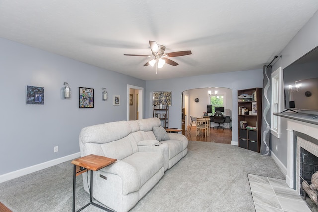 living area featuring a tiled fireplace, arched walkways, a ceiling fan, and light colored carpet