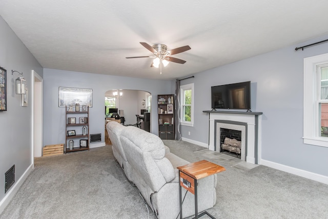 living area featuring arched walkways, carpet floors, ceiling fan, visible vents, and a fireplace with flush hearth