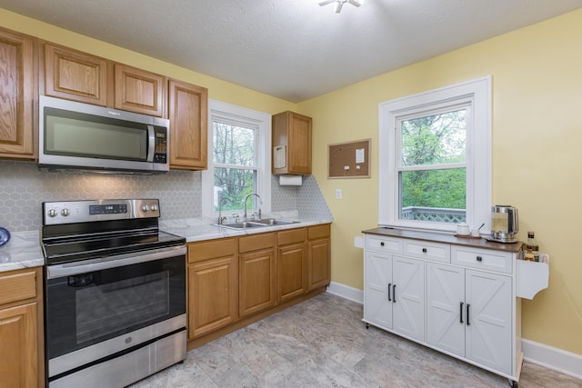 kitchen featuring tasteful backsplash, a sink, stainless steel appliances, light countertops, and baseboards