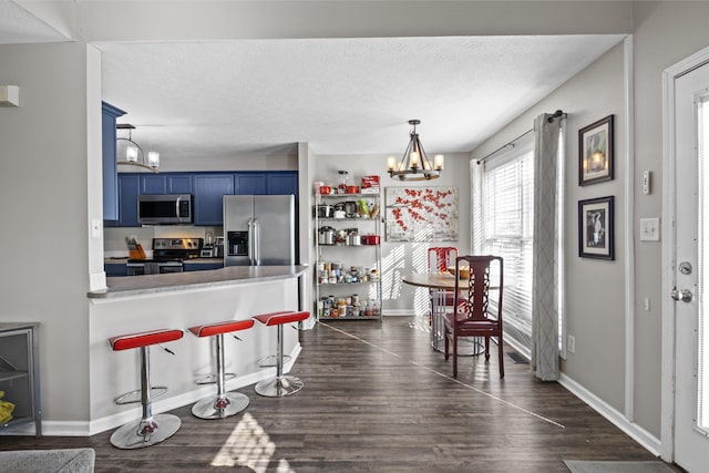 kitchen featuring a kitchen breakfast bar, dark wood-style floors, a chandelier, blue cabinets, and stainless steel appliances