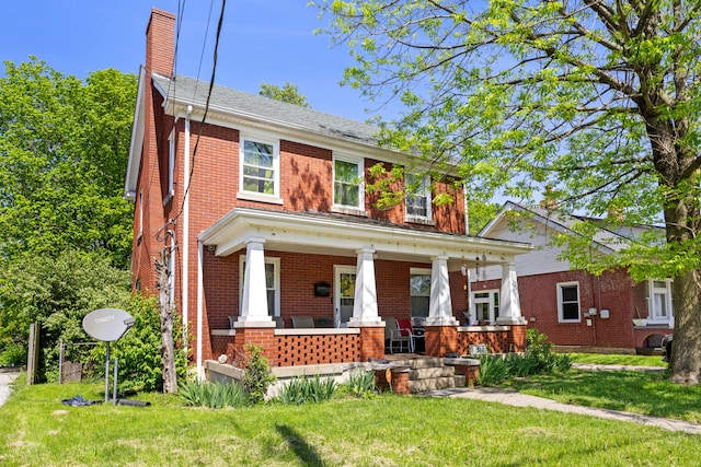 view of front of home with covered porch, brick siding, a chimney, and a front yard