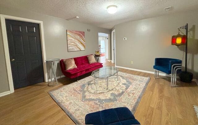 living area with wood finished floors, a textured ceiling, and baseboards