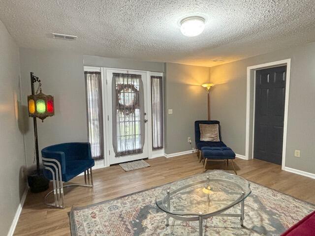 living area featuring visible vents, baseboards, wood finished floors, and a textured ceiling
