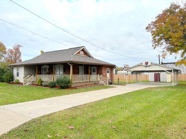 view of front facade featuring fence, a front lawn, driveway, covered porch, and a carport