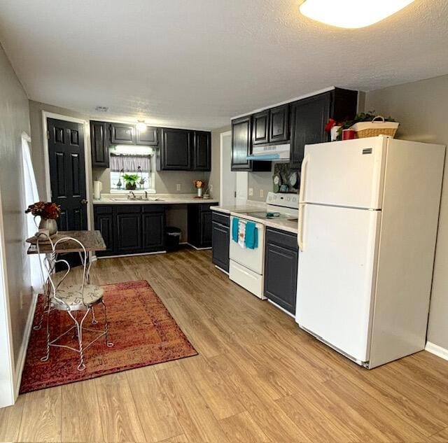 kitchen featuring a sink, white appliances, light wood finished floors, light countertops, and under cabinet range hood