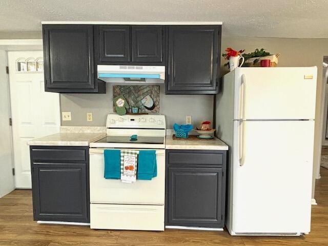 kitchen featuring wood finished floors, under cabinet range hood, light countertops, and white appliances