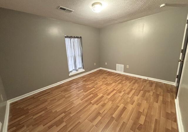 empty room with a textured ceiling, wood finished floors, and visible vents