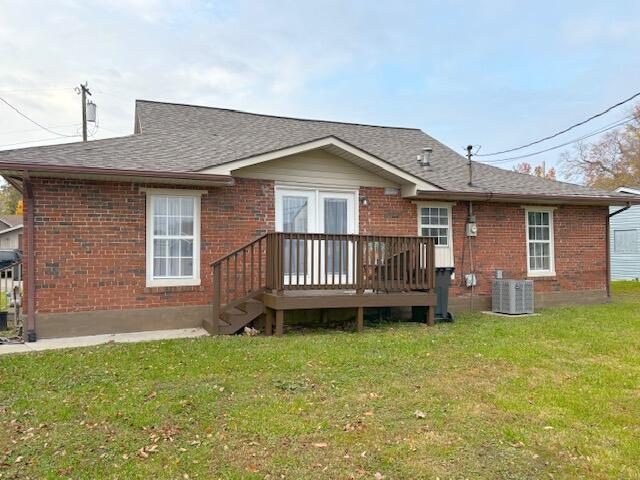 back of property featuring central AC unit, a shingled roof, a yard, a wooden deck, and brick siding