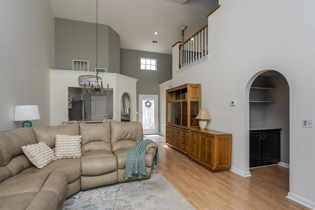 living room featuring arched walkways, a towering ceiling, a chandelier, light wood-type flooring, and baseboards