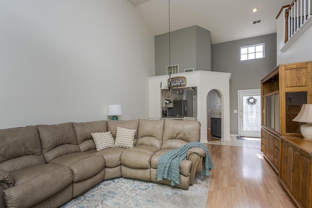 living room with a towering ceiling, arched walkways, light wood-type flooring, baseboards, and a chandelier