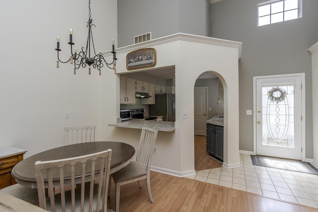 dining space featuring a towering ceiling, arched walkways, light wood-type flooring, baseboards, and a chandelier