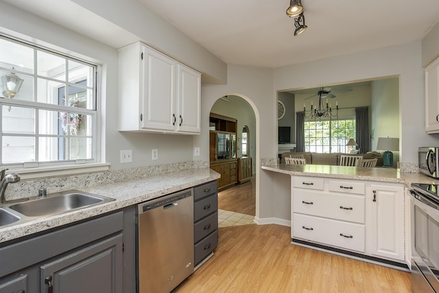 kitchen with appliances with stainless steel finishes, gray cabinets, light wood finished floors, a sink, and arched walkways