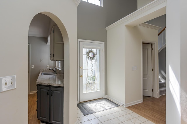 entryway with arched walkways, light wood finished floors, and baseboards