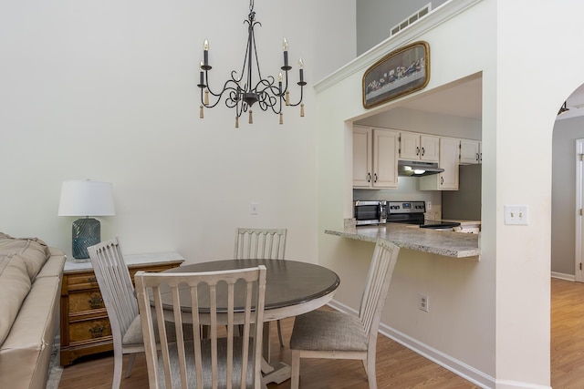 dining room with a chandelier, light wood finished floors, baseboards, and arched walkways