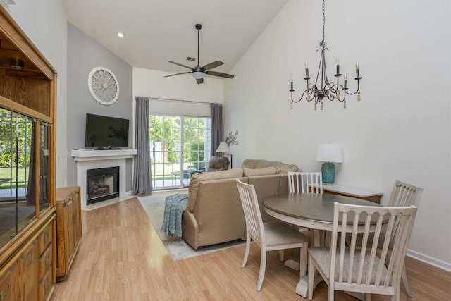 dining area featuring high vaulted ceiling, ceiling fan, light wood-style flooring, a fireplace with flush hearth, and a chandelier