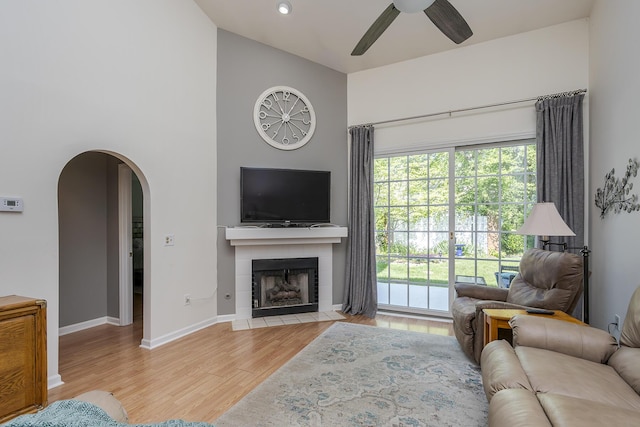 living room featuring a ceiling fan, a high ceiling, wood finished floors, arched walkways, and baseboards