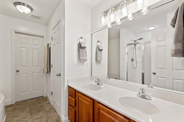 bathroom featuring visible vents, a stall shower, double vanity, and a sink