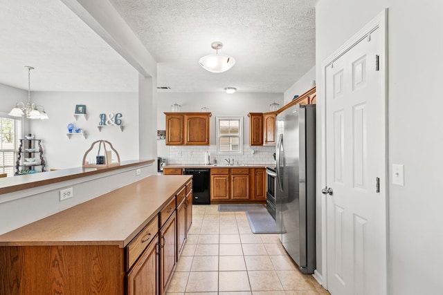 kitchen with brown cabinets, a sink, a notable chandelier, backsplash, and appliances with stainless steel finishes