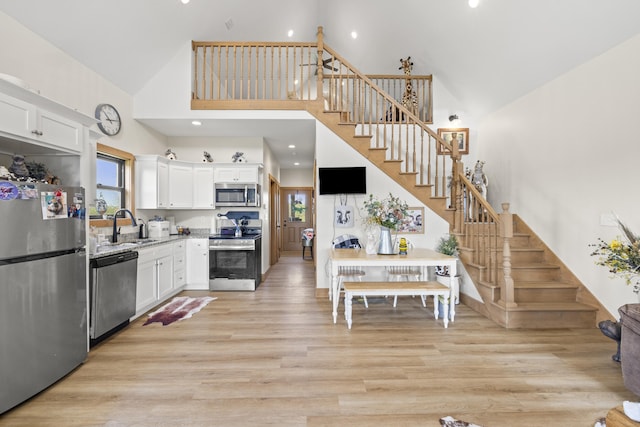 kitchen with a sink, light wood-style floors, high vaulted ceiling, white cabinetry, and appliances with stainless steel finishes