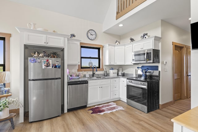 kitchen featuring light stone counters, white cabinets, a sink, appliances with stainless steel finishes, and light wood-type flooring