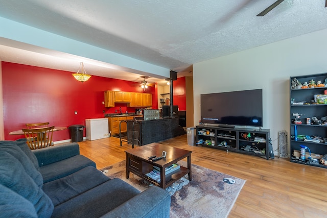 living room featuring a ceiling fan, a textured ceiling, and light wood-style floors