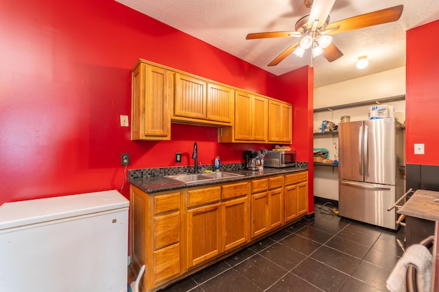 kitchen featuring dark countertops, ceiling fan, brown cabinets, a sink, and stainless steel appliances