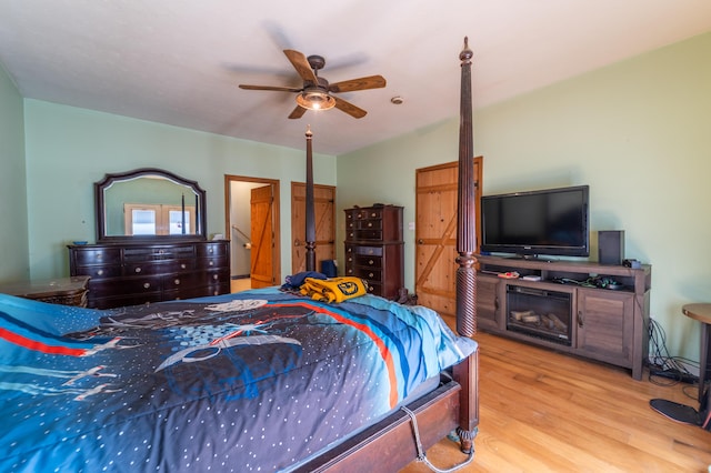 bedroom featuring a ceiling fan, wood finished floors, and a fireplace
