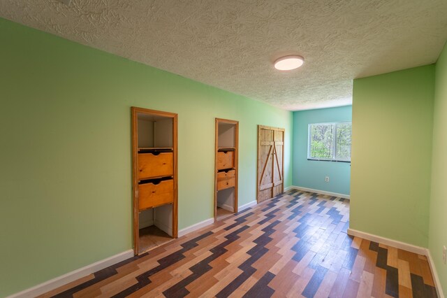 unfurnished bedroom featuring baseboards, a textured ceiling, two closets, and wood finished floors