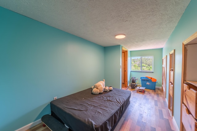 bedroom with a textured ceiling, baseboards, billiards, and wood finished floors