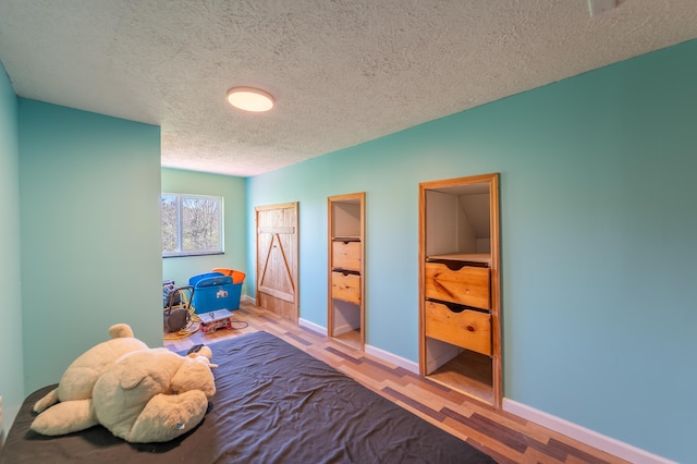 bedroom featuring baseboards, a textured ceiling, and wood finished floors