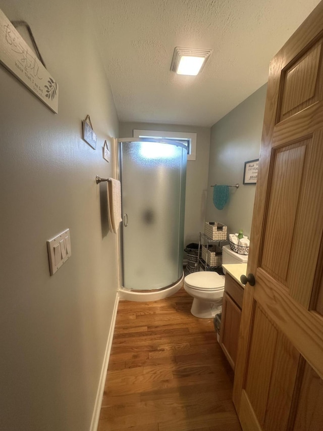 full bathroom with vanity, toilet, a textured ceiling, wood finished floors, and a stall shower