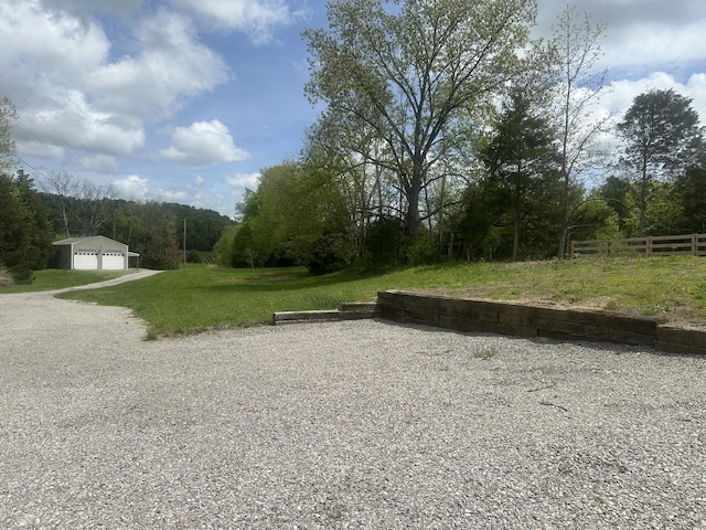 view of yard with a detached garage, a forest view, fence, and an outbuilding