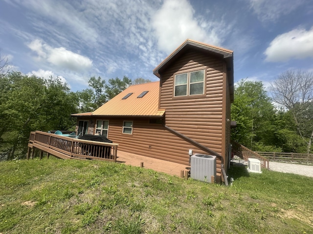 back of property featuring a wooden deck, faux log siding, central air condition unit, fence, and a yard