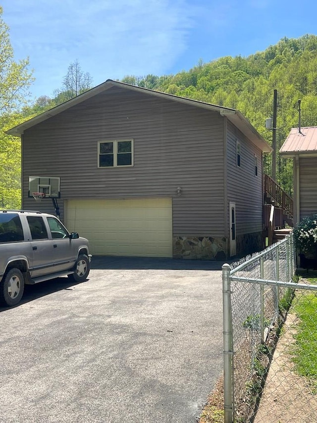 view of property exterior with fence, a garage, aphalt driveway, and stone siding